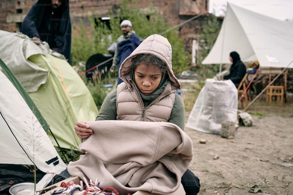 A child holding a blanket at a temporary shelter encampment